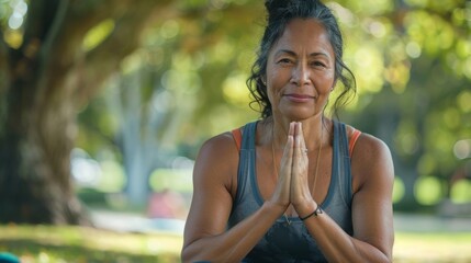 Wall Mural - Woman in tank top hands clasped in prayer sitting in park with trees blurred in background.