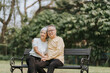 © Wicitr - Happy old couple sitting on chairs in the park arms around shoulders