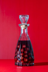 Wall Mural - Homemade cherry brandy in glass bottle on a red background, closeup