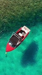 Wall Mural - Aerial footage of a small motorboat floating on a turquoise crystal clear transparent water. Kefalonia, Ionian sea, Greece. Drone orbit shot. Tourist speed boat moored near the beach. View from above