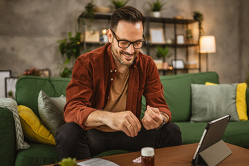 Adult man sit on sofa and prepare to drink medical pills at home