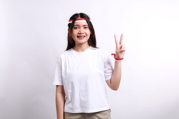 Asian young woman with red white ribbon for celebrating Indonesia independence day standing while showing two fingers