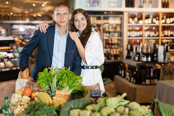 Wall Mural - Adult couple is standing with cart with products in the supermarket