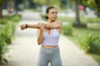 © DragonImages - Young woman in athletic wear stretching her arm while exercising outdoors in a sunny park setting