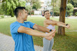 © DragonImages - Man and woman in athletic wear warming up together by stretching their arms during an outdoor exercise in the park