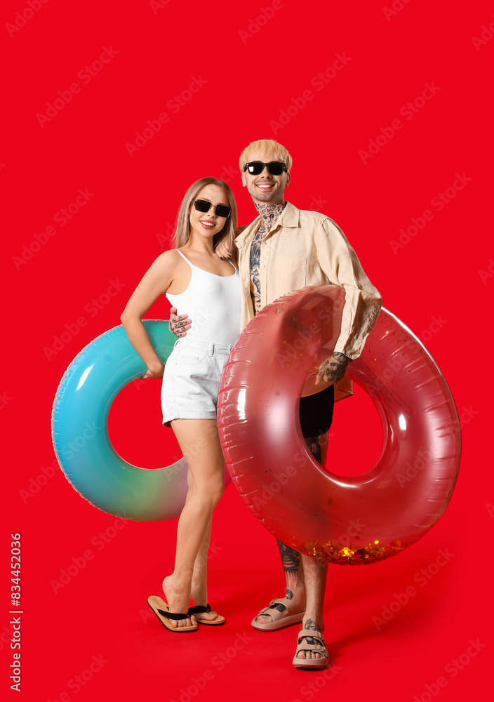 Young couple with inflatable rings on red background