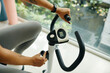 © DragonImages - Close-up shot of a woman adjusting the settings on an exercise bike, focusing on the hands and controls