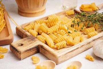 Wall Mural - Wooden board with uncooked fusilli pasta and thyme on light background, closeup