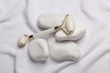 Wall Mural - Jade facial roller with pebbles on white towel. Beauty concept. Top view