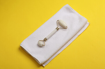 Wall Mural - Jade facial roller with towel on yellow background. Beauty concept