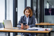 © David - Young busy smart serious Asian Japanese business woman executive holding cellphone device using mobile cell phone looking at smartphone working in corporate office with laptop computer technology.