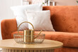 © Pixel-Shot - Basket with golden watering can on wooden coffee table in living room, closeup