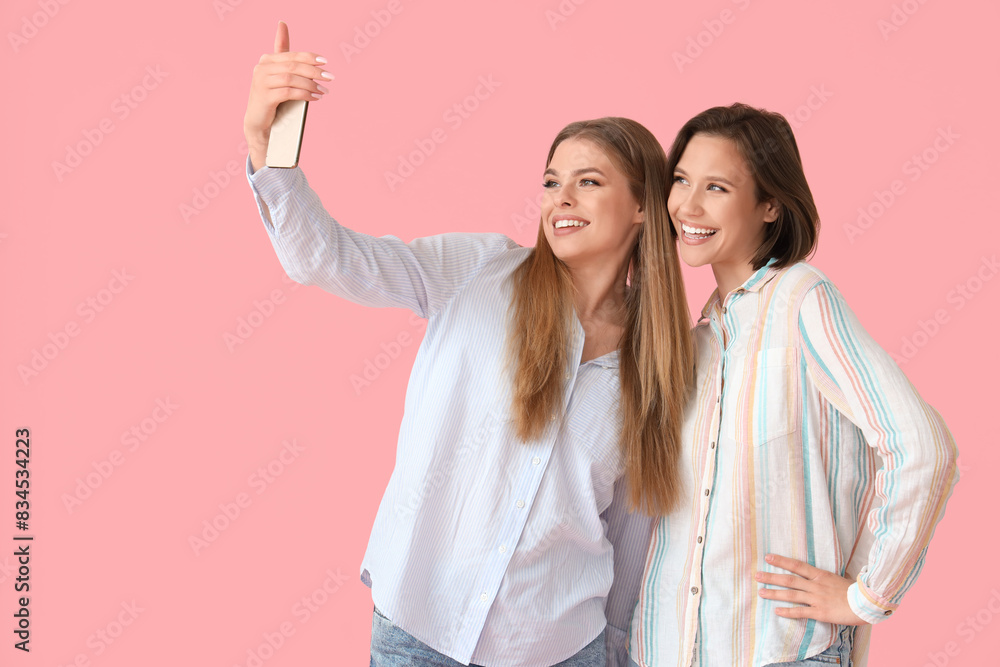 Female friends with mobile phone taking selfie on pink background