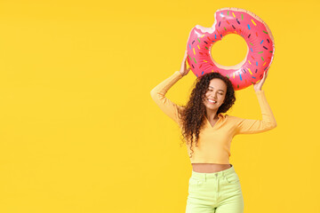 Wall Mural - Beautiful young African-American woman with inflatable ring on yellow background