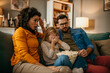 © La Famiglia - Family of three holding a popcorn pot and watching a scary movie together in the living room