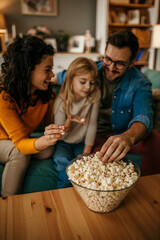 Wall Mural - Cheerful family Sitting in the living room and eating the popcorns