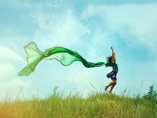 A woman in a grass field reaching towards a flowing green scarf against a blue sky, embodying freedom and joy. Generative AI