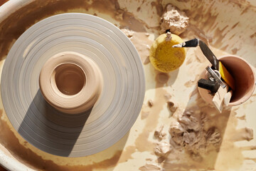 Wall Mural - Top view background image of well-used pottery wheel in sunlight with unfinished clay piece on top