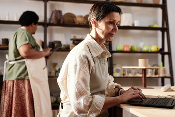 Wall Mural - Side view portrait of mature woman using computer in art studio and managing small business copy space