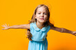 © SHOTPRIME STUDIO - Joyful little girl in a blue dress spreading her arms wide on a vibrant orange backdrop