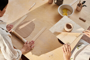 Wall Mural - High angle shot of two women shaping clay on wooden table in pottery class copy space