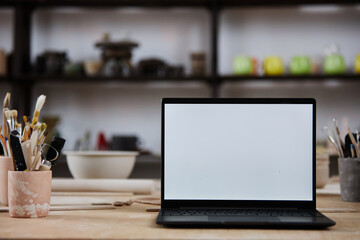Wall Mural - Background image of open laptop with blank white screen on wooden table in pottery studio, copy space