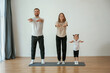 © standret - Warm up exercises. Family of mother, father and daughter are doing yoga at home