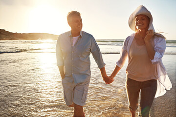 Senior, happy couple and holding hands with relax on beach sunset for support, love or bonding in nature. Man, woman or lovers walking with smile on outdoor summer holiday by water or ocean coast
