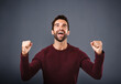 © peopleimages.com - Happy man, fist pump and winning with celebration for good news, vote or review on a blue studio background. Excited male person, young model or winner in hooray for success, victory or achievement