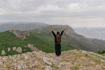 Wall Mural - A woman stands on a mountain top, holding two poles and smiling