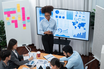 Wall Mural - Young african businesswoman presenting data analysis dashboard on TV screen in modern meeting. Business presentation with group of business people in conference room. Concord
