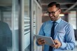 © Grigor - A businessman in a blue shirt and tie using a digital tablet in the office.