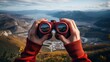 © MINHO - Both hands of a hiker use binoculars to see the view from a bird's eye view on a mountain.