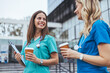 © Dragana Gordic - Two smiling female nurses in blue scrubs relax with coffee cups during a break outside a medical facility, enjoying a moment of camaraderie.