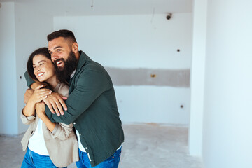 a beaming caucasian man and woman embrace in their spacious, just-purchased apartment, symbolizing a