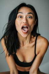 A woman with long black hair and a black sports bra is looking at the camera with her mouth open and tongue out