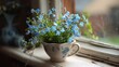 © LKT - A charming arrangement of delicate forget-me-not flowers, with their tiny blue blooms, displayed in a quaint ceramic teacup on a cozy windowsill. The whimsical and dainty flowers symbolize true love