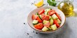 © Fotema - Tomato and cucumber salad with olive oil and lemon juice in a bowl on a grey background. Quarter of lemon, parsley, and olive oil behind. Copy space.