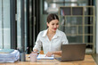 © apichat - A woman is sitting at a desk with a laptop and a clipboard