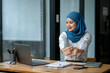 © apichat - A woman wearing a blue scarf is stretching her arms in front of a laptop