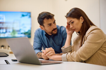 Distraught coworkers talking after receiving bad news via e-mail ins office.