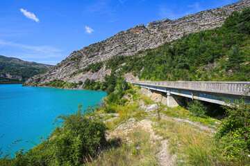 road bridge parallel to the shore of the lake of castillon in the southern alps in france - this res