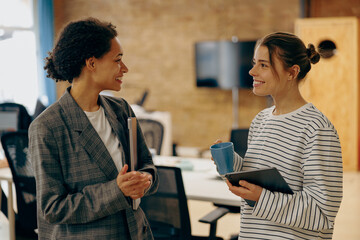 Wall Mural - Smiling women colleagues speak laughing enjoy leisure time at workplace. Corporate culture concept