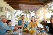 © GR/peopleimages.com - Cheers, wine and happy family on patio for lunch celebration, eating and bonding together at table. Children, men and women toast with glass, drinks and food in backyard for holiday, fun and relax