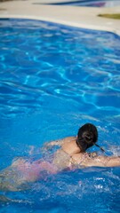 Wall Mural - A woman finding relaxation swimming in an outdoor pool under the sun on a sunny day