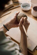 © AnnaStills - Vertical high angle shot of hands of unrecognizable artisan using clay carving tool to decorate handmade ceramic bowl