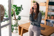 © Dorde - Smiling businesswoman talking on the phone while standing in a home office or a co-working space.