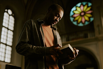 Wall Mural - Low angle view medium shot of African American man standing in Catholic church reading religious text in book