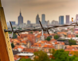 An abstract depiction of barbed wire set against a blurry city backdrop