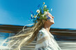 © stefanholm - A young Swedish woman with long blonde hair, wearing a traditional white linen dress with embroidery details and a vibrant Midsummer flower crown made of wildflowers like bluebells and daisies.